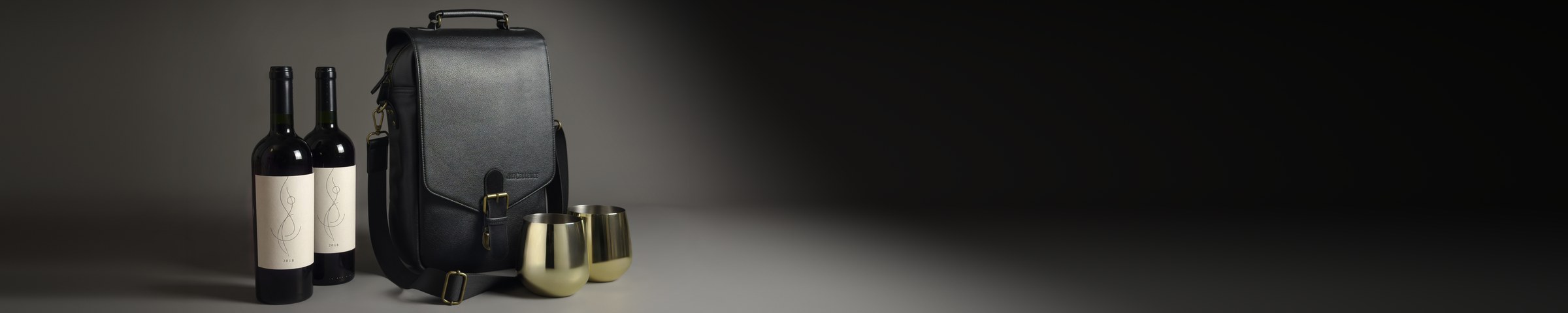 Black Artcellence wine carrier with two bottles and two gold steel glasses in a grey studio